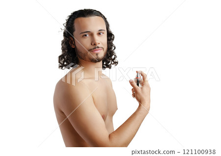 A young man with curly hair applying fragrance after a shower while smiling at the camera 121100938