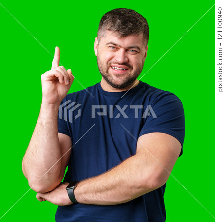 A man with a friendly smile gestures upwards while wearing a navy shirt against a bright green background A man with a friendly smile gestures upwards while wearing a navy shirt against a bright green background 121100940