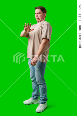 Young man making a disgusted expression while standing against a bright green background 121100960