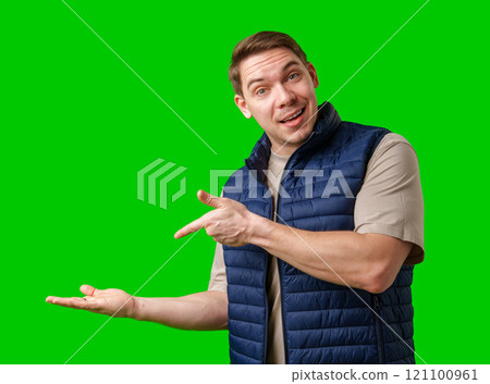 Man in a navy vest gestures while standing against a bright green background 121100961