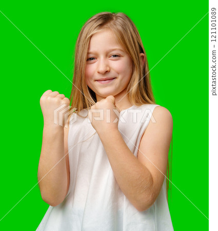 A young girl celebrating success with a joyful expression and clenched fists against a vibrant green background 121101089