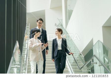 Men and women in suits walking down the stairs in an office 121101653