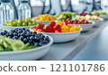 A vibrant variety of fresh fruits is beautifully arranged on a long table in a bright setting. 121101786