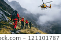 In a dramatic landscape shrouded in mist, climbers in bright red gear move cautiously uphill while a rescue helicopter hovers nearby, ready to assist in a daring operation among the rugged mountains. 121101787