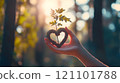 A hand gently holds a vibrant green sapling surrounded by a heart-shaped mass of moss, evoking a profound connection to nature. 121101788