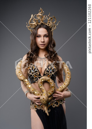 Model poses elegantly with a snake in ornate gold and black attire Model poses elegantly with a snake in ornate gold and black attire 121102268