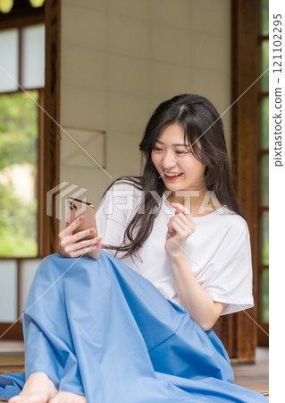 A young woman typing on her smartphone on the veranda of an old house. A young woman enjoying online shopping. 121102295