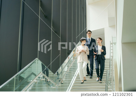 Men and women in suits walking down the stairs in an office 121102301