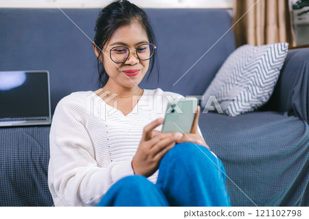 Selective focus, Happy young woman sitting on sofa enjoy using mobile phone for online shopping cashless in living room at home, Holding smartphone, reading good news in unexpected message or email. 121102798