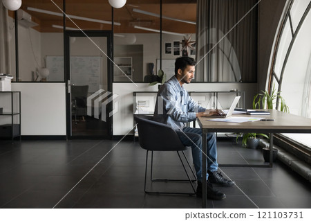 Focused Indian employee analyzing data, or writing emails on laptop 121103731