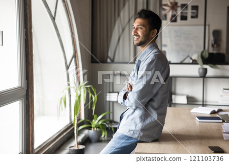Smiling Indian businessman looking out window with optimistic expression Smiling Indian businessman looking out window with optimistic expression 121103736