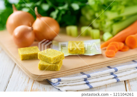 chicken bouillon cubes and fresh vegetables for soup on white wooden table, selective focus. chicken bouillon cubes and fresh vegetables for soup on white wooden table, selective focus. 121104261