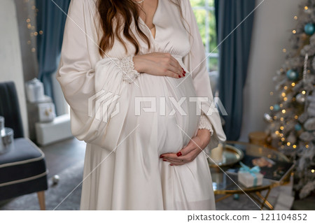 Pregnant woman holding a belly against Christmas tree with lights. family holiday concept. 121104852