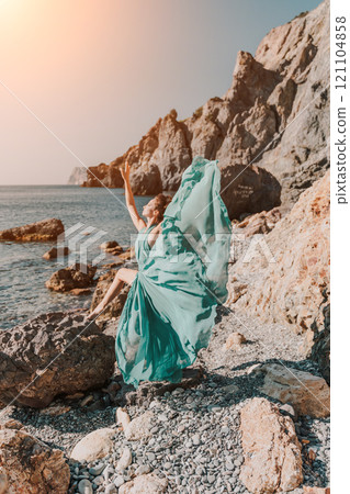Woman green dress sea. Woman in a long mint dress posing on a beach with rocks on sunny day. Girl on the nature on blue sky background. 121104858