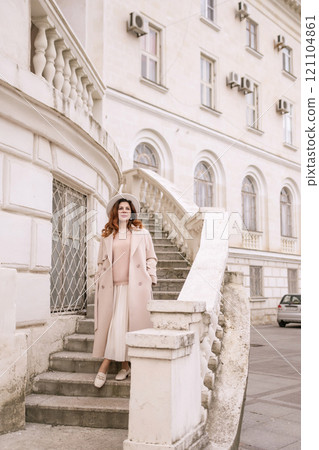 woman in elegant coat and hat against an intricate architectural backdrop, harmoniously blending modern fashion with historical allure. The soft daylight adds to its timeless appeal. woman in elegant coat and hat against an intricate architectural backdrop, harmoniously blending modern fashion with historical allure. The soft daylight adds to its timeless appeal. 121104861