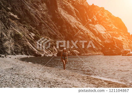 Woman travel summer sea. A happy tourist in a blue bikini enjoying the scenic view of the sea and volcanic mountains while taking pictures to capture the memories of her travel adventure. Woman travel summer sea. A happy tourist in a blue bikini enjoying the scenic view of the sea and volcanic mountains while taking pictures to capture the memories of her travel adventure. 121104867