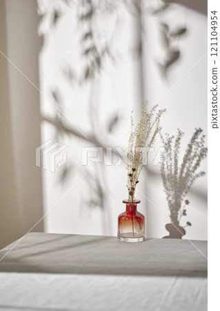 Warm sunlight streaming in through the window, beige background, flowers, vases, and a table with plants. Harmony of light and shadow. 121104954