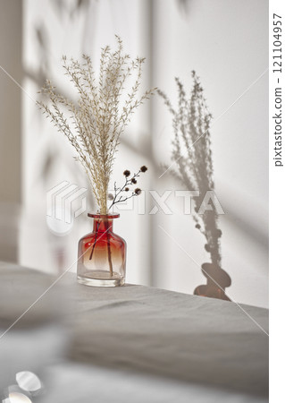 Warm sunlight streaming in through the window, beige background, flowers, vases, and a table with plants. Harmony of light and shadow. 121104957