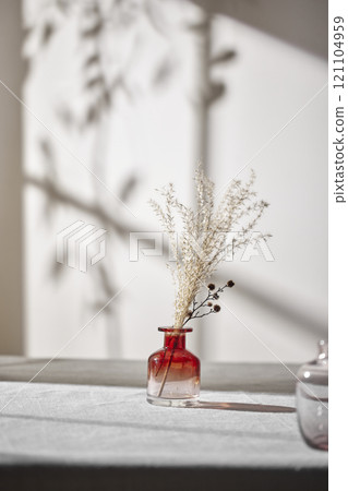 Warm sunlight streaming in through the window, beige background, flowers, vases, and a table with plants. Harmony of light and shadow. 121104959