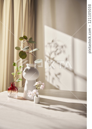 Warm sunlight streaming in through the window, beige background, flowers, vases, and a table with plants. Harmony of light and shadow. Warm sunlight streaming in through the window, beige background, flowers, vases, and a table with plants. Harmony of light and shadow. 121105038