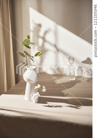 Warm sunlight streaming in through the window, beige background, flowers, vases, and a table with plants. Harmony of light and shadow. 121105046