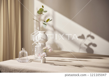 Warm sunlight streaming in through the window, beige background, flowers, vases, and a table with plants. Harmony of light and shadow. 121105047