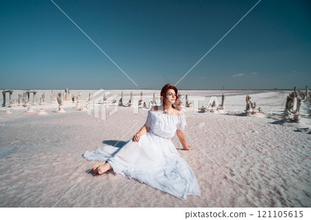 Woman White Dress Salt Flats Landscape - A woman in a white dress sits on the white salt flats under a clear blue sky. 121105615
