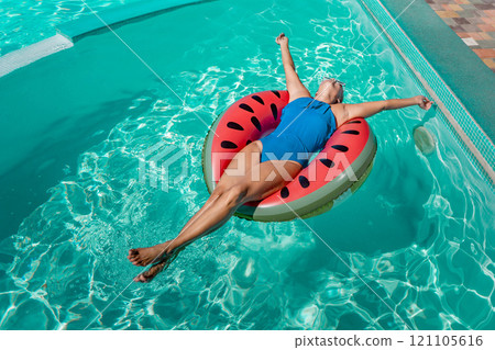 Happy woman in a swimsuit and sunglasses floating on an inflatable ring in the form of a watermelon, in the pool during summer holidays and vacations. Summer concept. 121105616