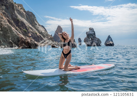 Woman sap sea. Sports girl on a surfboard in the sea on a sunny summer day. In a black bathing suit, he sits on a sapa in the sea. Rest on the sea. Woman sap sea. Sports girl on a surfboard in the sea on a sunny summer day. In a black bathing suit, he sits on a sapa in the sea. Rest on the sea. 121105631