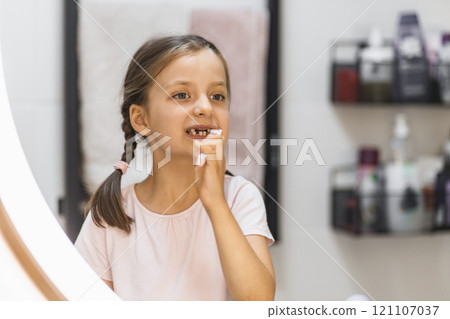 Caucasian girl brushing teeth and looking in mirror, sporting holes from missing milk teeth, in bathroom. Captures daily dental routine and childhood innocence. Caucasian girl brushing teeth and looking in mirror, sporting holes from missing milk teeth, in bathroom. Captures daily dental routine and childhood innocence. 121107037