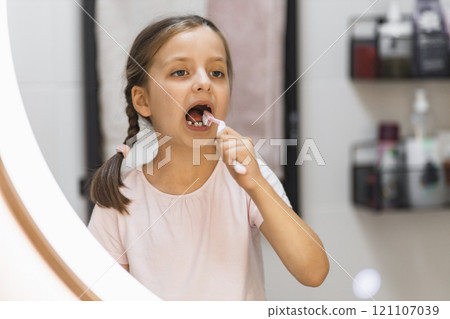 Caucasian girl with missing milk teeth brushing teeth in bathroom. She looks attentively in mirror, focusing on oral hygiene. Concept of childhood routines and dental care. Caucasian girl with missing milk teeth brushing teeth in bathroom. She looks attentively in mirror, focusing on oral hygiene. Concept of childhood routines and dental care. 121107039
