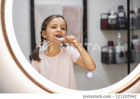 Portrait of young Caucasian girl with missing teeth brushing teeth while looking in bathroom mirror, emphasizing good oral hygiene habits. Portrait of young Caucasian girl with missing teeth brushing teeth while looking in bathroom mirror, emphasizing good oral hygiene habits. 121107042