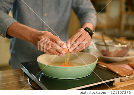 Close up of hands cracking an egg into a frying pan on an electric stovetop 121107276