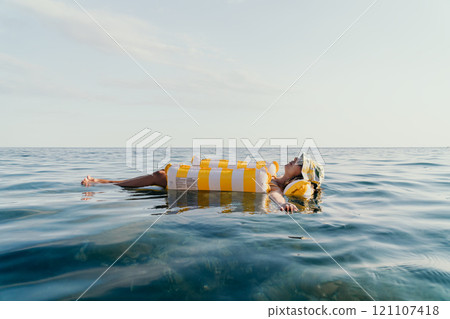 Woman Inflatable Float Relaxing Ocean - A woman relaxes on an inflatable float in the ocean on a sunny day. 121107418