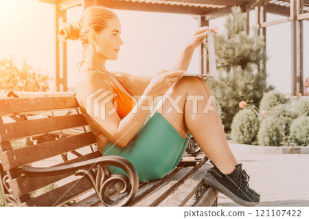 Woman, Laptop, Park: Young female athlete using laptop while sitting on a bench outdoors. Woman, Laptop, Park: Young female athlete using laptop while sitting on a bench outdoors. 121107422