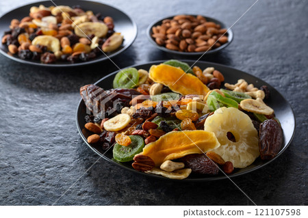 Dried tropical fruits, nuts, and raisins in black plate. 121107598