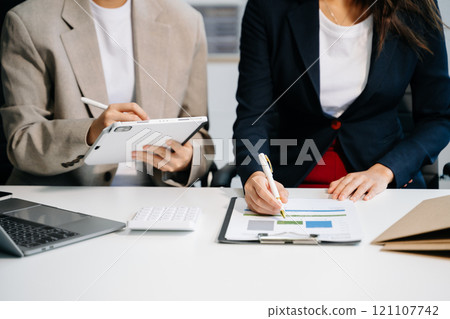 Business documents on office table with smart phone and calculator digital tablet and graph business with social network diagram and two colleagues discussing data working 121107742