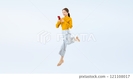 Full-body photo of a woman jumping while looking at her smartphone 121108017