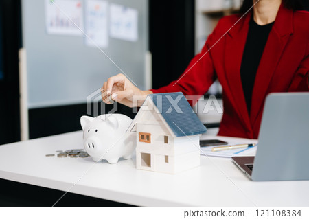 Young real estate agent worker working with laptop and tablet at table in office and small house beside it. Young real estate agent worker working with laptop and tablet at table in office and small house beside it. 121108384