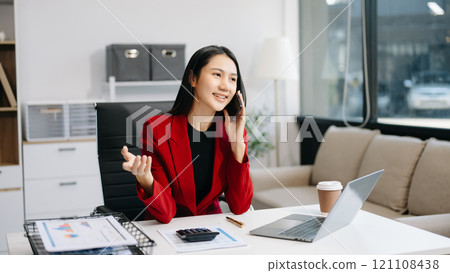 Asian Businesswoman Analyzing Finance on Tablet and Laptop at modern Office Desk tax 121108438