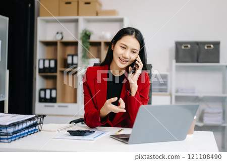 Asian Business woman Talking on the phone and using a laptop with a smile while Asian Business woman Talking on the phone and using a laptop with a smile while 121108490