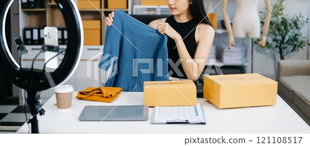 Fashion blogger concept, Young Asian women selling clothes on video streaming.Startup small business SME, using smartphone or tablet taking receive and checking 121108517