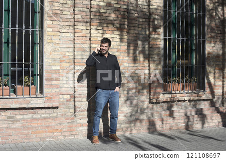 Man laughing while talking on the phone against a brick wall. 121108697