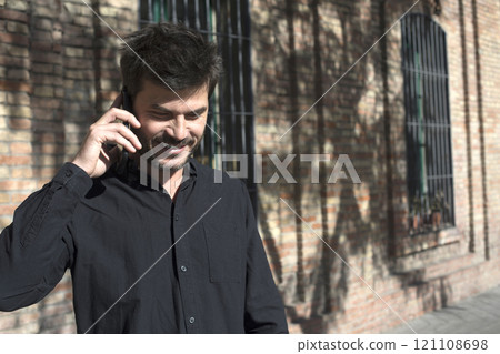 Man laughing while talking on the phone against a brick wall. 121108698
