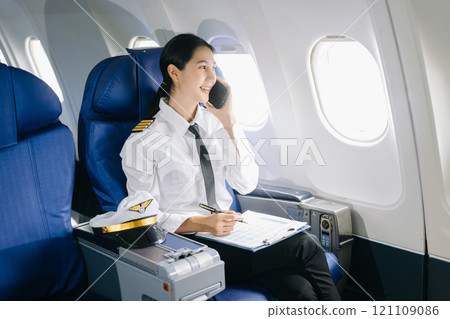 Asian Confident Feale pilot in uniform leaning at the passenger seat while standing inside of the airplane flight cockpit during takeoff Asian Confident Feale pilot in uniform leaning at the passenger seat while standing inside of the airplane flight cockpit during takeoff 121109086
