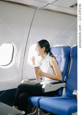 ttractive Asian female passenger of airplane sitting in comfortable seat while working laptop and tablet in style, work with grace. 121109198
