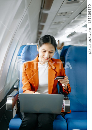 Attractive Asian female passenger of airplane sitting in comfortable seat while working laptop and tablet with mock up area using wireless connection. Attractive Asian female passenger of airplane sitting in comfortable seat while working laptop and tablet with mock up area using wireless connection. 121109570