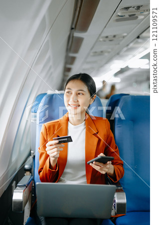 Asian businesswoman or entrepreneur in a formal suit on an airplane sitting in business class using a phone, computer laptop. Travel in style, work Asian businesswoman or entrepreneur in a formal suit on an airplane sitting in business class using a phone, computer laptop. Travel in style, work 121109571