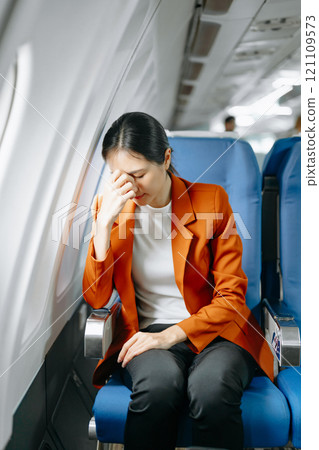 Photo of a frustrated woman sitting on an airplane with her head in her hands. Asian woman sitting 121109573