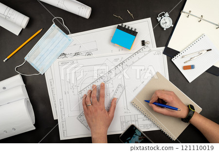 Mechanical drawing on sheets of paper. Hands on the table top view. Workflow of an architect, engineer. Write and draw. Ruler, pencil, notebook 121110019